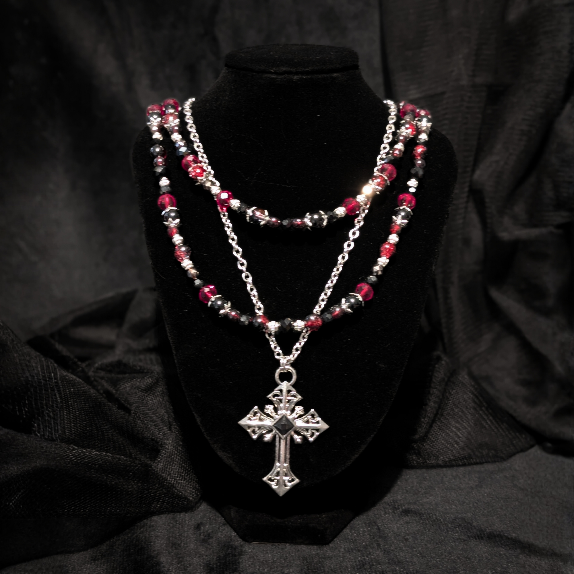 Gothic necklace with a large cross on a silver chain with other red and black beaded chains above